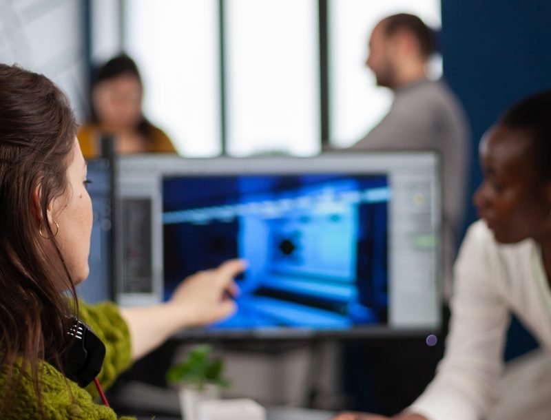 Gamer creator explaning to african worker how testing game level interface, developing new design in creative office pointing at screen. Player online video games with technology network wireless.